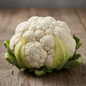Large dense white cauliflower curd with green outer leaves on rustic wooden surface