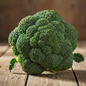 Large dense green broccoli head with tight florets on rustic wooden surface, fresh and vibrant