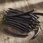 Long slender dark purple-black French bean pods on rustic wooden surface in natural sunlight